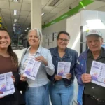 Quatro pessoas seguram panfletos da campanha Junho Violeta dentro de uma loja de eletrodomésticos no bairro Carneirinhos, em João Monlevade. A ação faz parte das atividades de conscientização sobre o combate à violência contra a pessoa idosa e a divulgação de seus direitos.