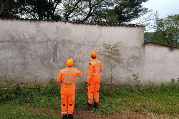 Imagem mostra dois bombeiros militares uniformizados observando uma área próxima a um muro no bairro Feixos, em João Monlevade. A equipe atuou na avaliação e eliminação de um enxame de abelhas que representava risco para participantes, organizadores e público de um evento esportivo realizado na região.