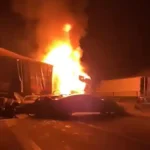 Acidente na BR-381 durante a noite, com caminhão em chamas após colisão envolvendo outros veículos. Carros danificados aparecem na pista enquanto o fogo intenso ilumina a rodovia.