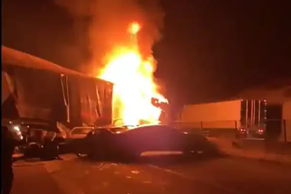 Acidente na BR-381 durante a noite, com caminhão em chamas após colisão envolvendo outros veículos. Carros danificados aparecem na pista enquanto o fogo intenso ilumina a rodovia.