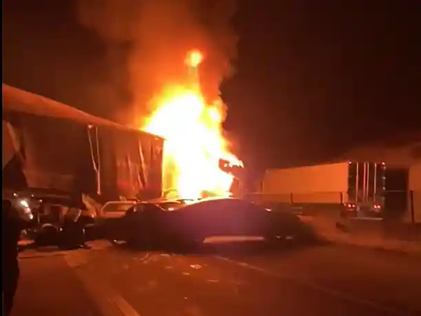 Acidente na BR-381 durante a noite, com caminhão em chamas após colisão envolvendo outros veículos. Carros danificados aparecem na pista enquanto o fogo intenso ilumina a rodovia.