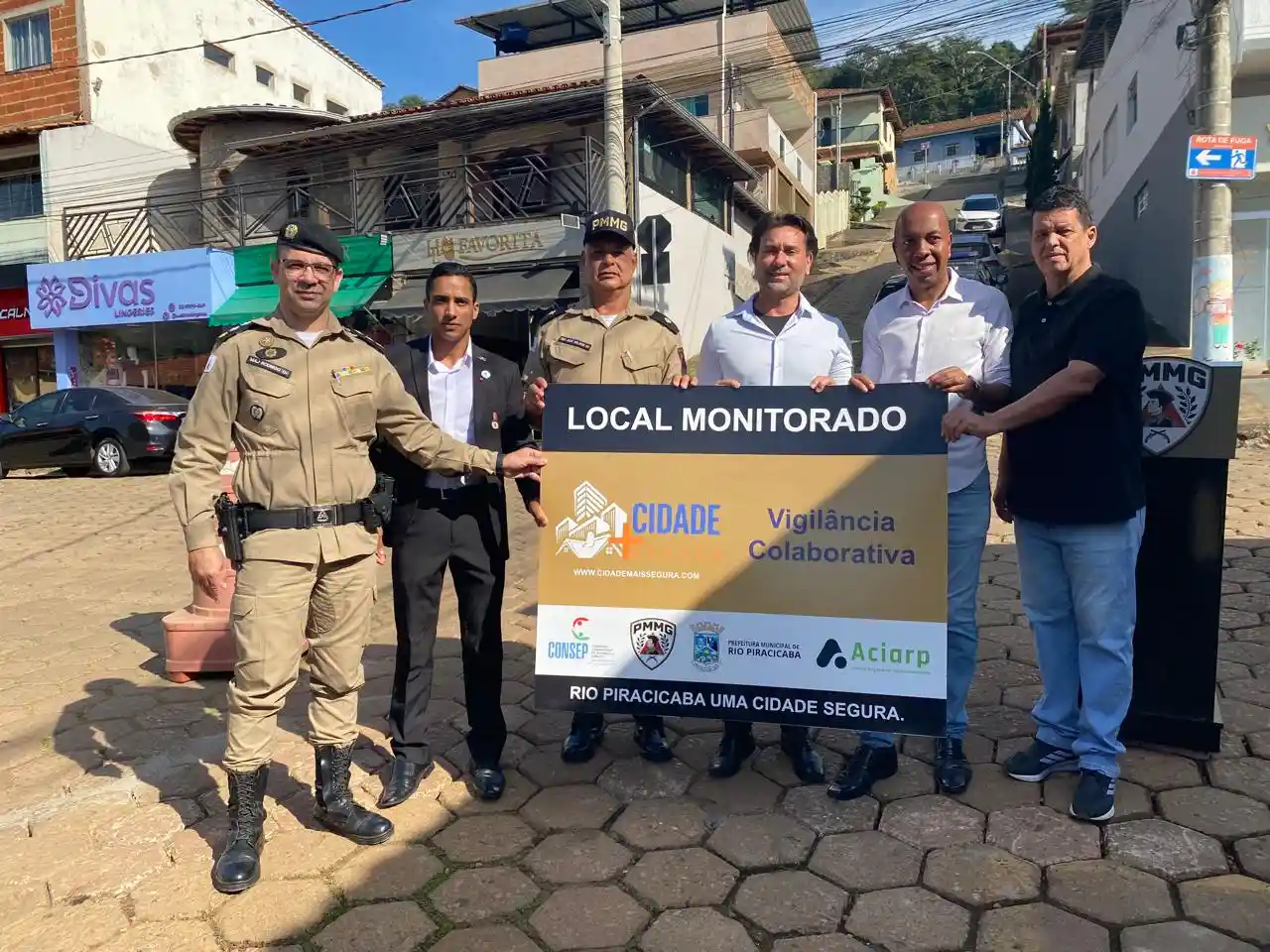 Autoridades municipais, policiais militares e representantes da ACIARP posam em uma rua do Centro de Rio Piracicaba segurando uma placa do Projeto Vigilância Colaborativa. A ação marca a ampliação do sistema de videomonitoramento e reforça as medidas de segurança pública no município.