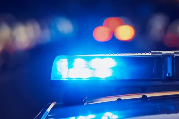 Luzes azuis de emergência acesas no teto de uma viatura policial durante a noite. A imagem ilustra uma ocorrência atendida pela Polícia Militar.