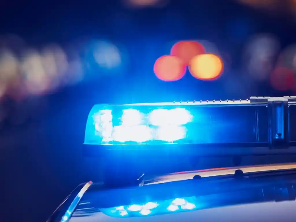 Luzes azuis de emergência acesas no teto de uma viatura policial durante a noite. A imagem ilustra uma ocorrência atendida pela Polícia Militar.