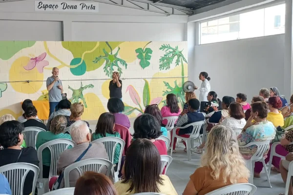Público acompanha cerimônia realizada na sede da Associação de Lavadeiras de Monlevade. Ao fundo, o Espaço Dona Preta recebe homenagem à fundadora da entidade, enquanto participantes assistem aos pronunciamentos durante a reinauguração do local após a conclusão das obras de reforma.