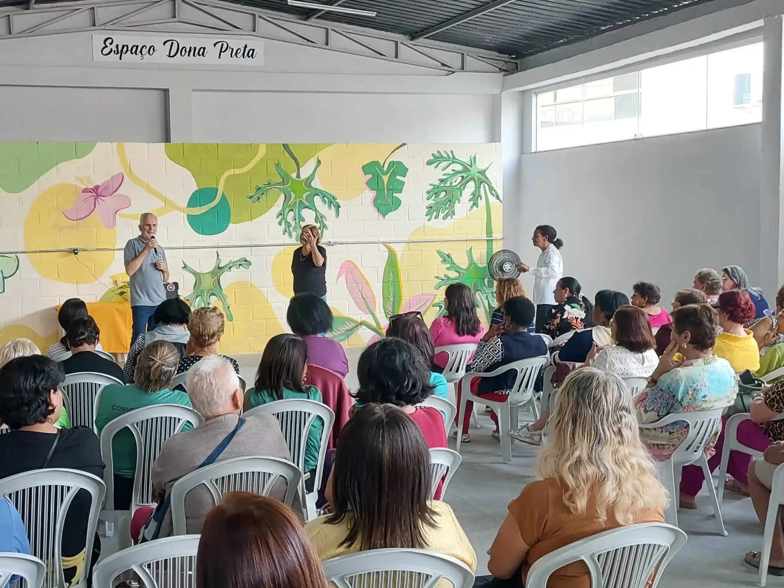 Público acompanha cerimônia realizada na sede da Associação de Lavadeiras de Monlevade. Ao fundo, o Espaço Dona Preta recebe homenagem à fundadora da entidade, enquanto participantes assistem aos pronunciamentos durante a reinauguração do local após a conclusão das obras de reforma.