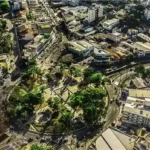 Imagem aérea do centro de Itabira, com ruas, prédios, praças e áreas arborizadas vistas de cima. A fotografia ilustra o cenário urbano da cidade e o contexto de obras públicas e projetos de infraestrutura voltados ao desenvolvimento municipal.