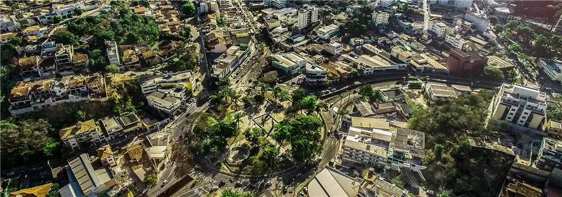 Imagem aérea do centro de Itabira, com ruas, prédios, praças e áreas arborizadas vistas de cima. A fotografia ilustra o cenário urbano da cidade e o contexto de obras públicas e projetos de infraestrutura voltados ao desenvolvimento municipal.
