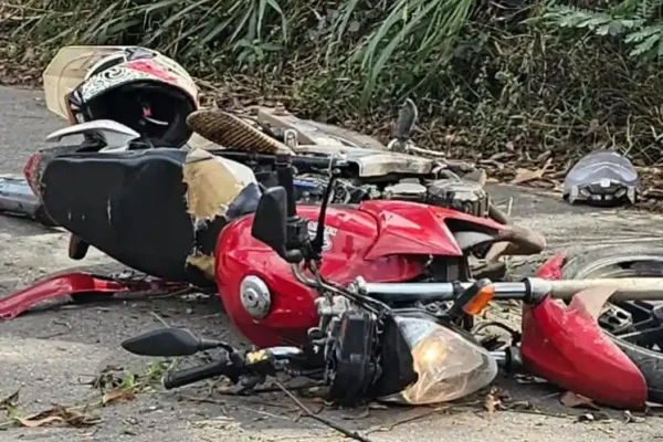 Motocicleta vermelha caída sobre o asfalto após acidente no bairro Campos Elíseos, em João Monlevade. Peças espalhadas pela pista e capacetes próximos ao veículo evidenciam os danos causados pela colisão.