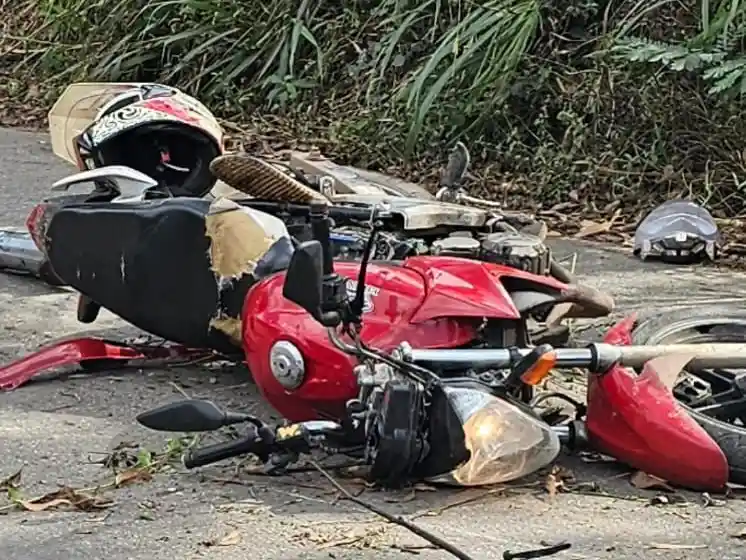 Motocicleta vermelha caída sobre o asfalto após acidente no bairro Campos Elíseos, em João Monlevade. Peças espalhadas pela pista e capacetes próximos ao veículo evidenciam os danos causados pela colisão.