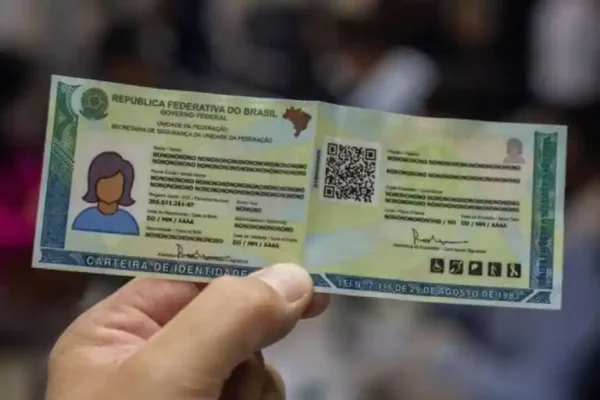 Mão segurando a nova Carteira de Identidade Nacional, que utiliza a identificação pelo CPF como registro único do cidadão. O documento exibe QR Code e elementos de segurança destinados à autenticação e ao acesso facilitado a serviços públicos.