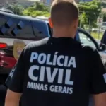 Policial com uniforme da Polícia Civil de Minas Gerais caminha próximo a viaturas oficiais durante uma operação. A fotografia ilustra uma ação policial relacionada à captura de um investigado e ao cumprimento de mandado de prisão.