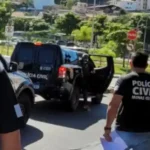 Policial com uniforme da Polícia Civil de Minas Gerais caminha próximo a viaturas oficiais durante uma operação. A fotografia ilustra uma ação policial relacionada à captura de um investigado e ao cumprimento de mandado de prisão.
