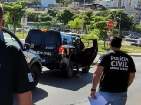 Policial com uniforme da Polícia Civil de Minas Gerais caminha próximo a viaturas oficiais durante uma operação. A fotografia ilustra uma ação policial relacionada à captura de um investigado e ao cumprimento de mandado de prisão.