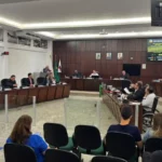 Imagem mostra os vereadores reunidos no plenário da Câmara Municipal durante sessão legislativa. Os parlamentares estão sentados em seus respectivos lugares enquanto acompanham a votação de projetos de lei. Ao fundo, um painel eletrônico exibe informações da reunião, e parte do público acompanha os debates nas cadeiras destinadas aos visitantes.