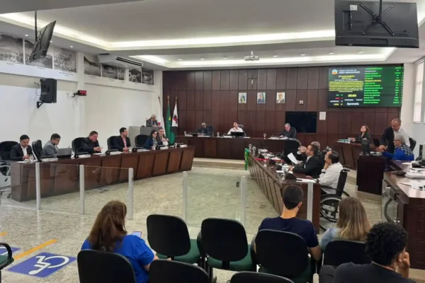 Imagem mostra os vereadores reunidos no plenário da Câmara Municipal durante sessão legislativa. Os parlamentares estão sentados em seus respectivos lugares enquanto acompanham a votação de projetos de lei. Ao fundo, um painel eletrônico exibe informações da reunião, e parte do público acompanha os debates nas cadeiras destinadas aos visitantes.