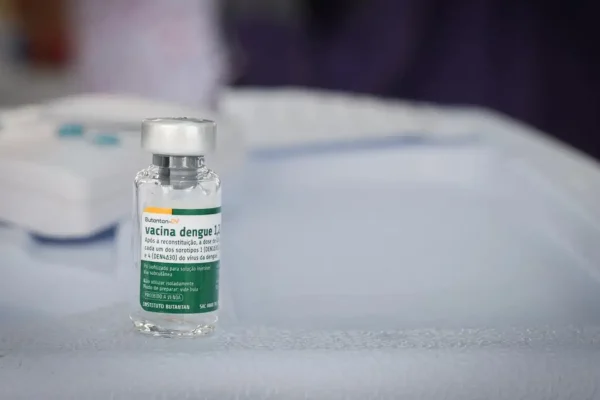 Frasco da vacina contra a dengue do Instituto Butantan em destaque sobre uma mesa. O imunizante teve a aplicação suspensa temporariamente pelo Ministério da Saúde após a investigação de casos de reações graves e duas mortes suspeitas.