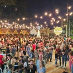 Grande público visita o Mercado de Natal organizado pela Casa de Cultura em João Monlevade, com chalés iluminados, decoração natalina, luzes suspensas e famílias circulando pelo evento durante a noite.