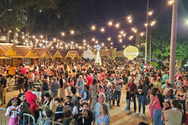 Grande público visita o Mercado de Natal organizado pela Casa de Cultura em João Monlevade, com chalés iluminados, decoração natalina, luzes suspensas e famílias circulando pelo evento durante a noite.