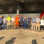 Foto mostra um grupo de autoridades, servidores municipais e integrantes do Corpo de Bombeiros e da Defesa Civil reunidos em frente às novas instalações dos serviços de emergência em João Monlevade. Ao fundo, aparecem viaturas do Corpo de Bombeiros estacionadas dentro da estrutura coberta da antiga Rodoviária, local que passa a integrar o futuro Centro de Urgência do município.