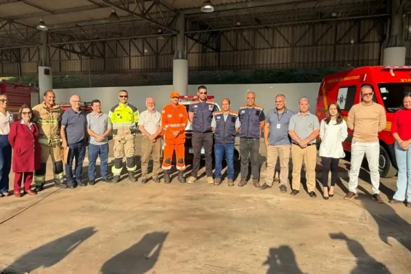 Foto mostra um grupo de autoridades, servidores municipais e integrantes do Corpo de Bombeiros e da Defesa Civil reunidos em frente às novas instalações dos serviços de emergência em João Monlevade. Ao fundo, aparecem viaturas do Corpo de Bombeiros estacionadas dentro da estrutura coberta da antiga Rodoviária, local que passa a integrar o futuro Centro de Urgência do município.