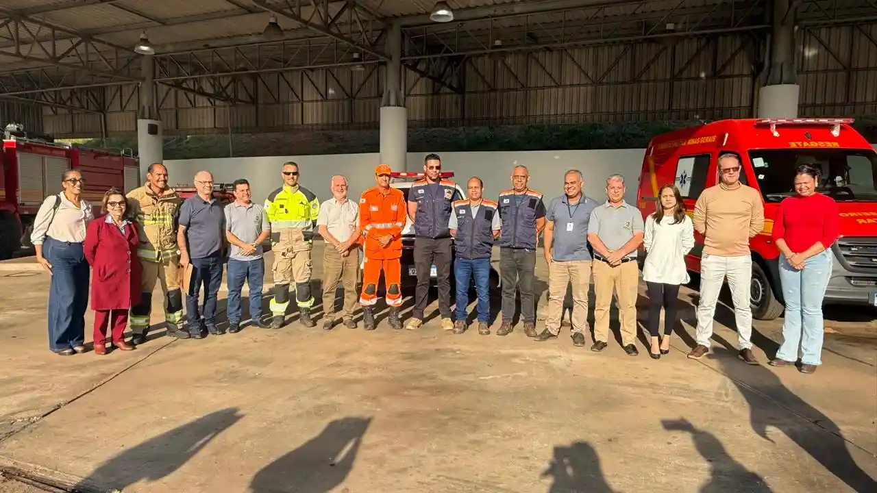 Foto mostra um grupo de autoridades, servidores municipais e integrantes do Corpo de Bombeiros e da Defesa Civil reunidos em frente às novas instalações dos serviços de emergência em João Monlevade. Ao fundo, aparecem viaturas do Corpo de Bombeiros estacionadas dentro da estrutura coberta da antiga Rodoviária, local que passa a integrar o futuro Centro de Urgência do município.