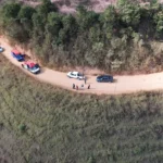 Imagem aérea mostra equipes do SAMU e dos Bombeiros Voluntários atendendo uma ocorrência em uma estrada de terra em São Domingos do Prata. Viaturas de resgate, carros parados e pessoas estão no local. O motociclista ferido foi estabilizado e levado ao Hospital Margarida, em João Monlevade, para avaliação médica.