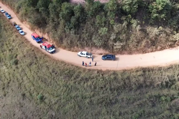 Imagem aérea mostra equipes do SAMU e dos Bombeiros Voluntários atendendo uma ocorrência em uma estrada de terra em São Domingos do Prata. Viaturas de resgate, carros parados e pessoas estão no local. O motociclista ferido foi estabilizado e levado ao Hospital Margarida, em João Monlevade, para avaliação médica.
