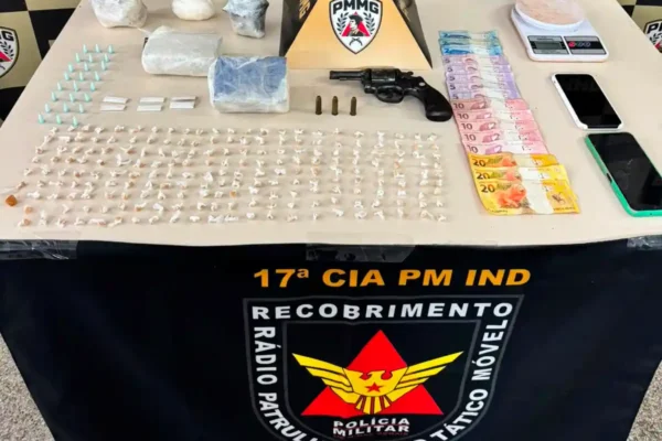 Mesa de exposição do Tático Móvel da Polícia Militar com drogas apreendidas, revólver calibre .38, munições, balança de precisão, celulares e dinheiro durante operação em João Monlevade.