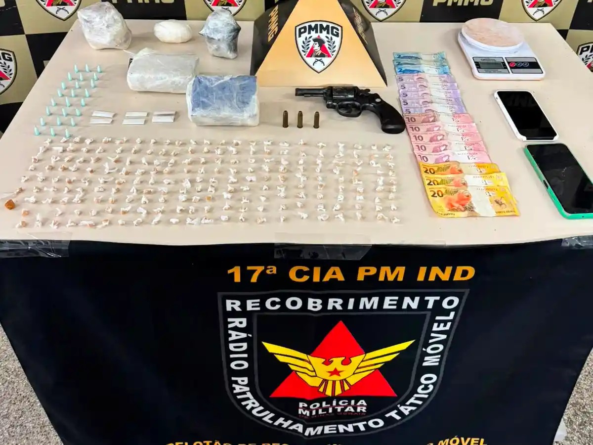Mesa de exposição do Tático Móvel da Polícia Militar com drogas apreendidas, revólver calibre .38, munições, balança de precisão, celulares e dinheiro durante operação em João Monlevade.