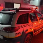 Viatura da Guarda Civil Municipal de Santa Bárbara com giroflex ligado, estacionada em frente à Delegacia de Plantão da Polícia Civil, em Itabira, durante registro de ocorrência policial.