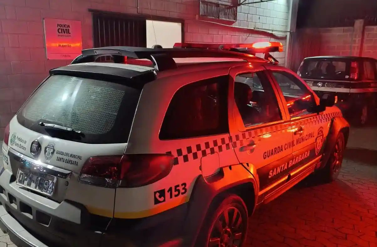 Viatura da Guarda Civil Municipal de Santa Bárbara com giroflex ligado, estacionada em frente à Delegacia de Plantão da Polícia Civil, em Itabira, durante registro de ocorrência policial.