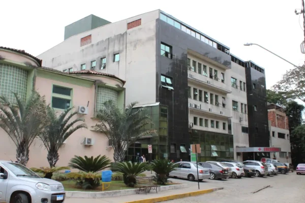Fachada do Hospital Margarida, em João Monlevade (MG), com edifício de vários andares, entrada do setor de emergência, carros estacionados e área ajardinada na parte frontal.