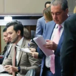 Parlamentares reunidos durante sessão da Assembleia Legislativa de Minas Gerais, com deputados analisando documentos no plenário. A imagem ilustra a votação do projeto que fixa teto para cachês artísticos e que será encaminhado ao governador de Minas Gerais para sanção.