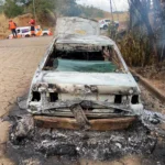 Carro Santana totalmente queimado após incêndio na BR-381, em Nova Era, com equipes do Corpo de Bombeiros e da Nova 381 atuando no local.