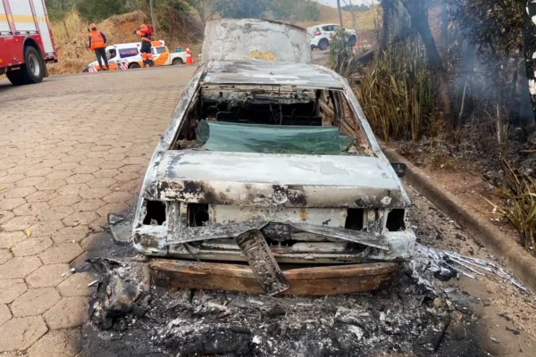 Carro Santana totalmente queimado após incêndio na BR-381, em Nova Era, com equipes do Corpo de Bombeiros e da Nova 381 atuando no local.