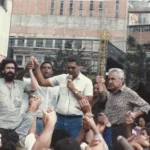 Greve de 1986 em João Monlevade com trabalhadores reunidos durante manifestação, levantando os braços em ato de mobilização e oração.